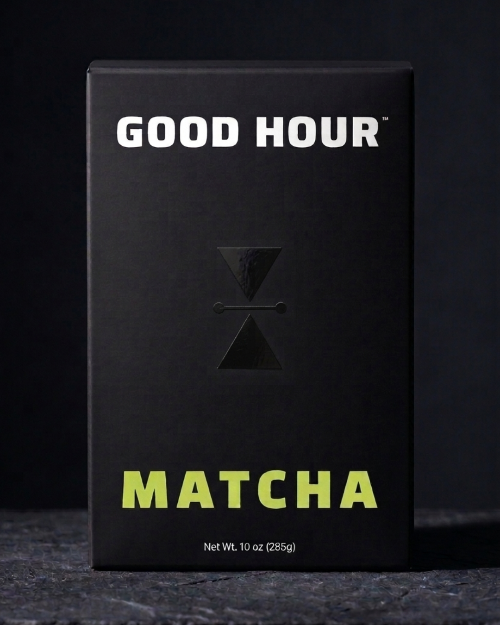 A black rectangular box of Good Hour Matcha with white 'GOOD HOUR' text at the top, a black hourglass logo in the center, and bright yellow-green 'MATCHA' text at the bottom, photographed against a dark background.